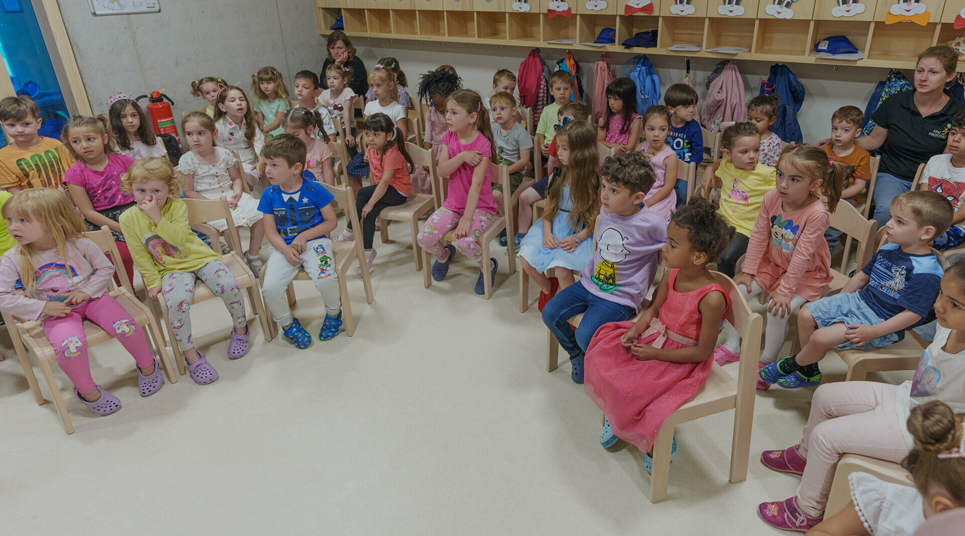 Viele Kinder sitzen in einem Raum in einem Stuhlkreis. 