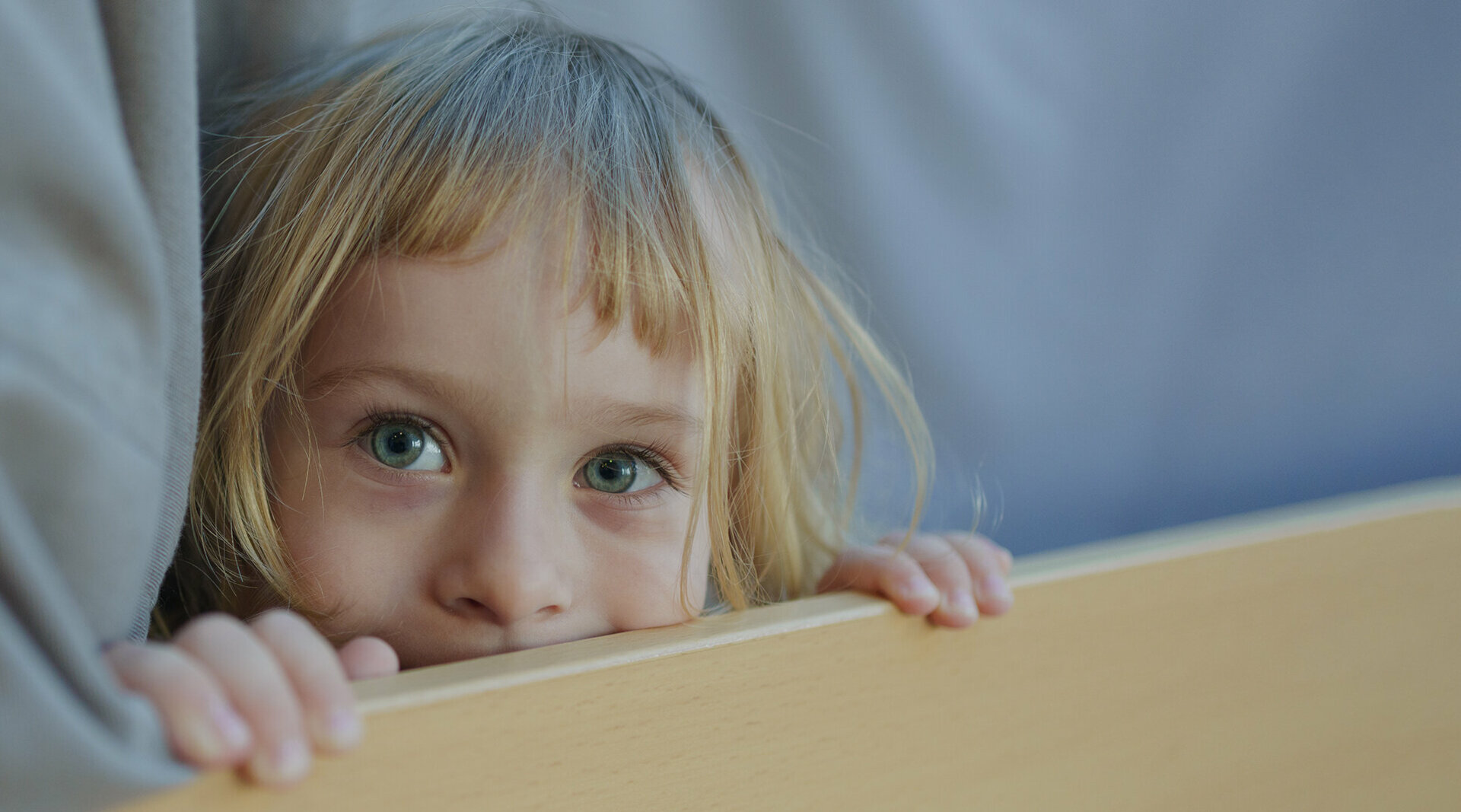 Ein Foto: Ein kleines Kind schaut neugierig über eine Tischkante. 